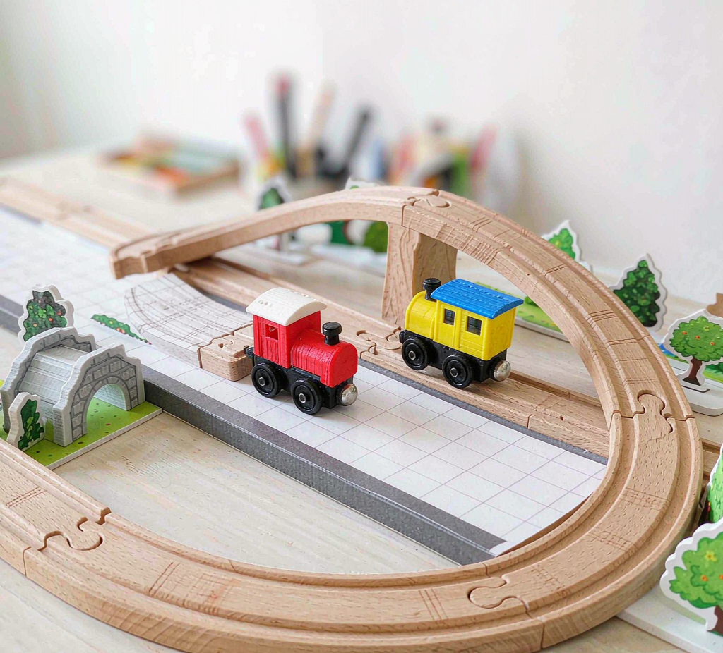 A wooden railway layout with printed station, bridge and trees