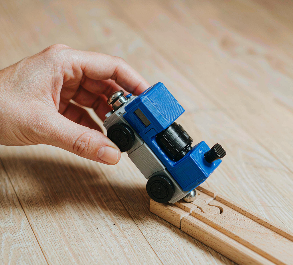 A 3D-printed tram being placed onto wooden railway track by hand